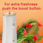 Close-up of the top of a Glade automatic dispenser with an arrow indicating the boost button and tropical foliage background.