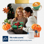 Two people exchanging a wrapped gift with Glade device and refill pack shown and festive pumpkin decorations