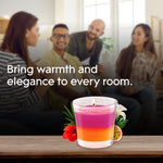 Lifestyle scene with a lit Glade pink-and-orange candle on a table in front of a blurred group of people and warm room text