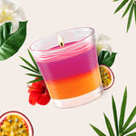 Close-up of a lit Glade spun jar candle with layered pink-orange wax, passionfruit halves and tropical foliage