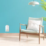 Modern teal living room wall with a white plugged-in air freshener device near a wooden armchair, lamp and plant.