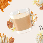 Tilted lit Glade jar candle with caramel and vanilla dessert accents on a pale background, showcasing the candle jar texture