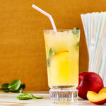 Glass of iced yellow drink with a red-striped flexible straw and a bundle of multicolored straws in a holder