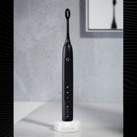 Black Gleem electric toothbrush standing on a white charging base in a bathroom setting