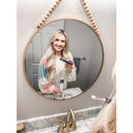 Smiling person seen in a round mirror holding a navy Gleem electric toothbrush in a bathroom