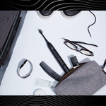 Flatlay of a black Gleem electric toothbrush with travel items and accessories on white surface