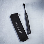 Black Gleem electric toothbrush beside a black zippered travel pouch on a light surface