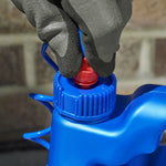 Close-up of a gloved hand gripping the red nozzle and blue cap of a plastic sprayer attached to a jug