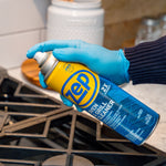 Gloved hand holding a Zep oven & grill cleaner can angled over a stovetop, ready to spray.