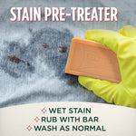 Gloved hand rubbing a Fels‑Naptha soap bar into a wet stain on fabric with instructional headline stain pre‑treater.