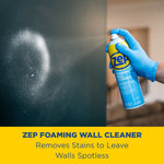 Gloved hand spraying Zep foaming wall cleaner can at a dark painted wall with product name banner below