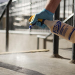 Gloved hand using a Zep professional spray bottle to apply mist near an outdoor railing or concrete surface.
