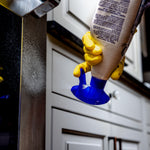 Gloved hand holding a Bar Keepers Friend spray bottle upside down, nozzle visible, in front of kitchen cabinet and appliance.