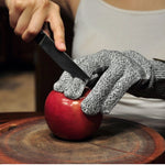Gloved hands slicing an apple on a wooden board wearing gray knit protective gloves