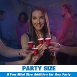 Woman smiling at a dimly lit party while several hands hold red mini shot cups toward her, with "PARTY SIZE" banner