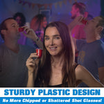 Smiling woman holding a single red mini shot cup at a lively party where others are drinking from similar tiny red cups