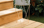 Gold metal plant stand placed on wooden steps with a planter visible above