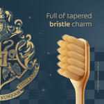 Close-up of a gold toothbrush head on a dark patterned background with Harry Potter crest artwork and 'Full of tapered bristle charm' text