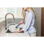 Lifestyle image of person using Goodcook Pro dish wand to wash a white plate at a kitchen sink with running faucet