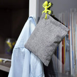 Gray fabric deodorizer pouch hung from a decorative green hook beside clothing