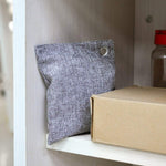 Gray woven fabric deodorizer pouch standing on a shelf next to a cardboard box