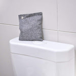 Gray fabric deodorizer pouch sitting on a toilet tank against tiled wall