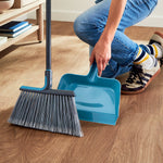 Lifestyle view of Great Value angle broom and teal dustpan on a wood floor with a person kneeling nearby