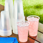 Two filled Great Value clear plastic cups with ice and pink beverage on a wooden table beside stacked empty cups