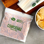 Staged scene of a filled translucent Great Value compostable gallon bag on a counter next to chips and folded bags