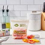 Styled kitchen scene with a filled Great Value compostable quart bag on a cutting board and sliced peppers nearby