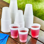 Stacks of white translucent disposable cups on a table with three cups filled with red drink in front