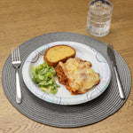 Prepared place setting with a Great Value patterned disposable plate holding lasagna, salad and garlic bread on a woven placemat