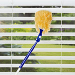 Blue-handled Great Value 360° duster cleaning horizontal window blinds with garden visible outside