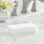 White rectangular cleaning eraser placed on a marble countertop near a bathroom faucet and a small vase of flowers.