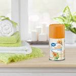 Single Great Value Hawaiian automatic air freshener spray refill on a wooden surface with towels and candles in soft-focus background