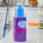 Great Value lavender-scent spray mop solution bottle placed on a kitchen counter with cleaning items blurred in background.