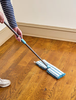 Person using a Great Value microfiber flip mop on a wood floor, showing the mop head, pole and part of the user's legs and shoes