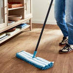 Lifestyle shot of a Great Value microfiber flip mop cleaning a wood floor near a low cabinet, showing the mop head and black handle