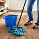 Room scene with a blue microfiber mop and bucket on a wood floor, showing a person's lower legs and sneakers.