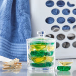 Clear glass jar filled with green and yellow laundry pacs, with towel and laundry basket blurred in background