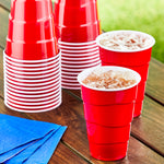 Stacked Great Value red plastic party cups and two filled red cups with ice on a wooden table next to blue napkins