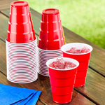 Stacked red disposable party cups on a wooden table with two filled red cups containing ice, napkins nearby