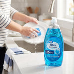 Kitchen lifestyle scene showing a Great Value Ultra Dish Liquid bottle on a counter while a person washes a plate at the sink
