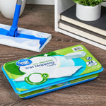 Stacked Great Value wet mopping cloth packages on a wood floor beside a mop and bookshelf, front product label visible