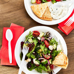 Lifestyle top-down scene of white plastic fork and spoon with salad plates and red napkins