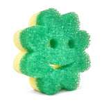 Close-up of a green flower-shaped Scrub Mommy dual-sided scrubber with smiling face and yellow sponge backing
