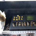 Open grill with a Range Kleen liner on the grates holding grilled asparagus, pineapple chunks and bacon-wrapped jalapeños.