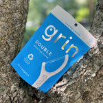 Blue Grin Double pouch propped in tree bark, photographed outdoors showing front packaging detail