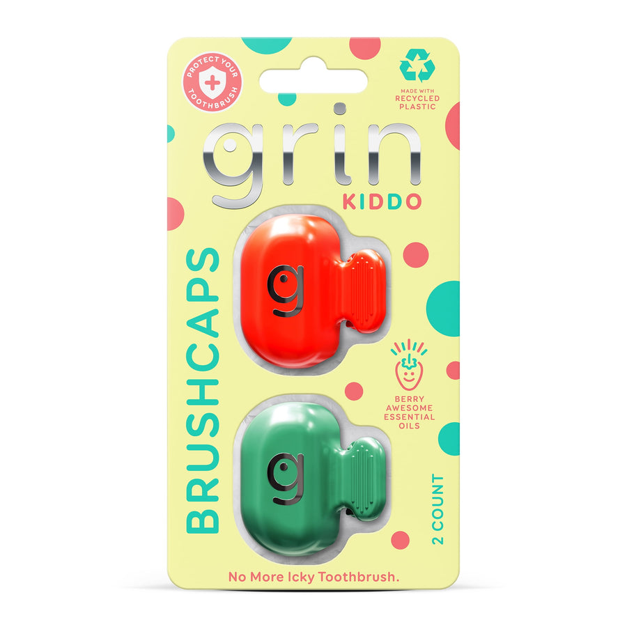 Retail blister card showing two colorful Grin Kiddo brushcap covers in red and green with playful polka-dot backing