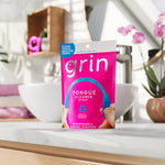 GRIN pink pouch standing on a bathroom counter in a bright lifestyle shot with sink and orchid in background